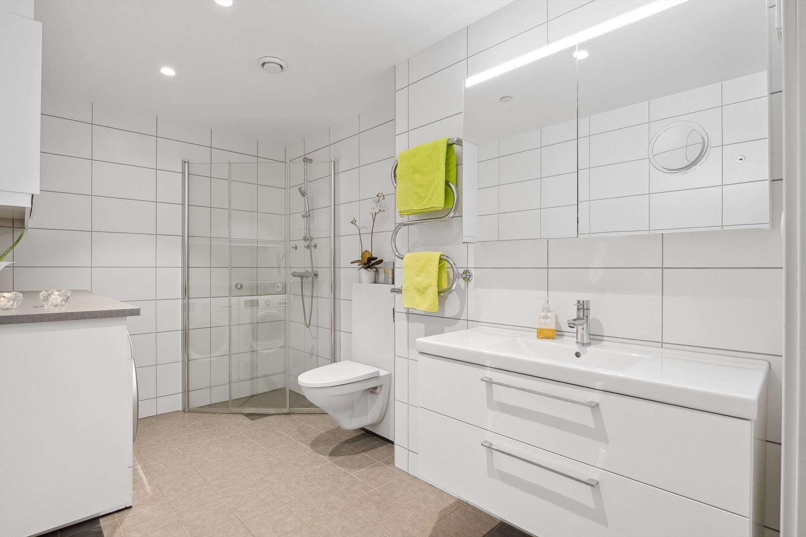 Rommet er innredet med praktisk og stilfull baderomsinnredning med servant og skuffseksjon, elektrisk håndkletørker for den ekte hotellfølelsen i hverdagen, vegghengt toalett og speilskap med belysning. Galleribilde