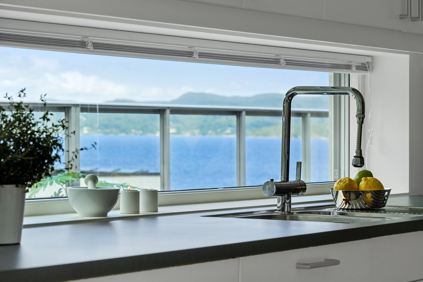 Videre byr kjøkkenet på detaljer som belysning under overskap, vask med påkostet kjøkkenservant, og overskap på en vegg og vindu mellom benkeplate og overskap som sikrer godt med dagslys med fantastisk sjøutsikt. Galleribilde