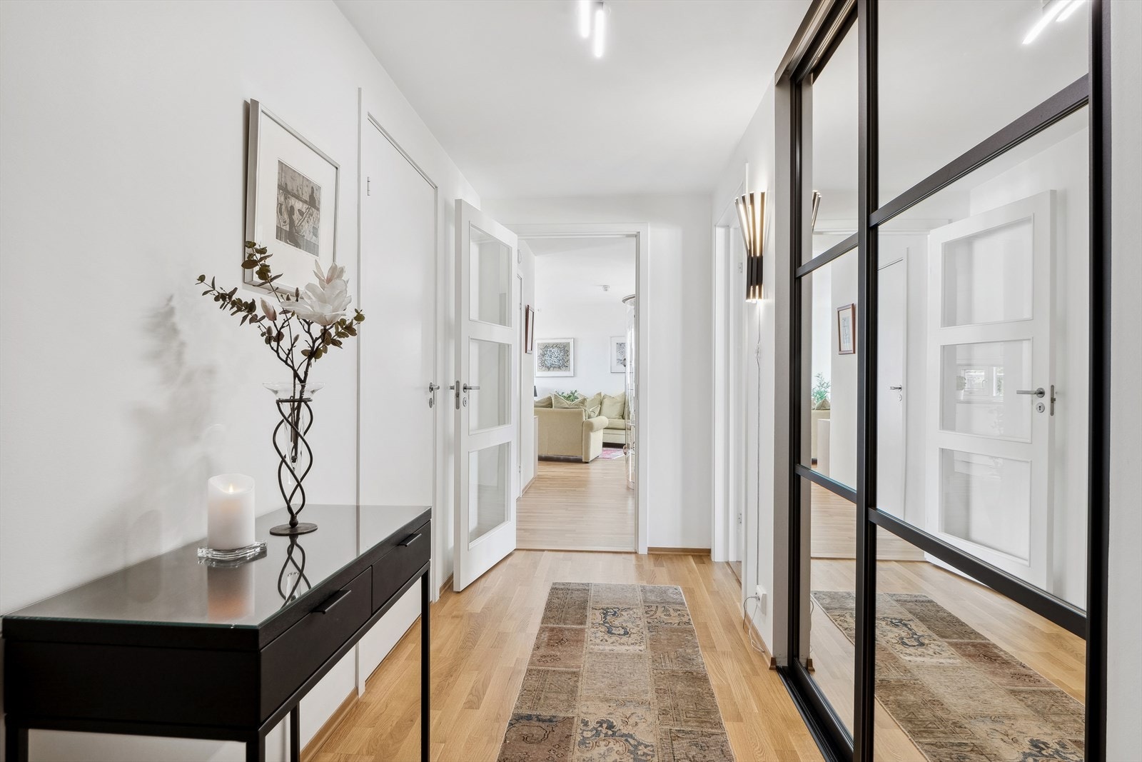 Vel innenfor inngangsdøren møtes man av en romslig og moderne entré med flott parkettgulv og praktisk skyvedørsgarderobe med speilfront og Elfa garderobesystem. Dør som adskiller stuen fra entreen har glass for fint lysinslipp i rommet. Galleribilde