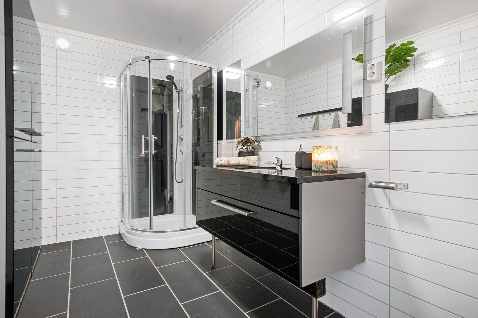 Badet er innredet med vegghengt toalett, glatte fronter, steinplate med underlimt vask, speil med lys, høyskap og dusjkabinett. Galleribilde
