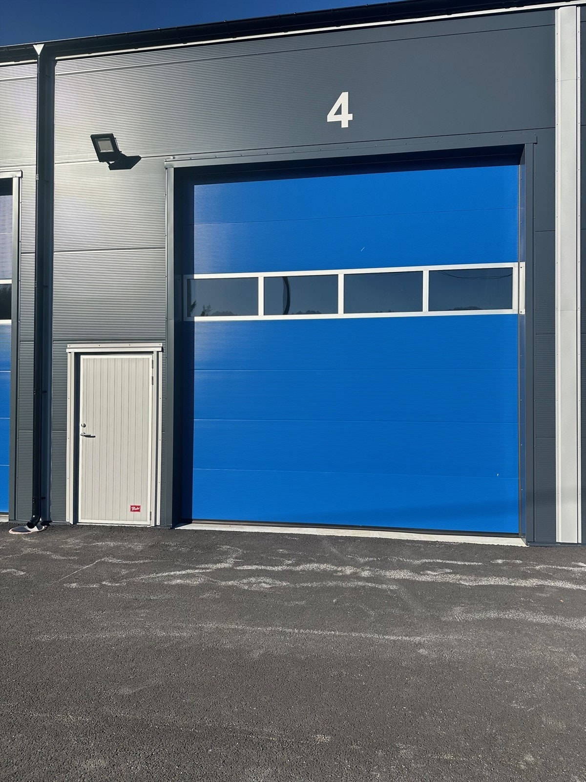 En elektrisk leddheisport med b x h = 4m x 4,4m pr. seksjon. Port leveres med vindu og en fjernkontroll. Bygget er isolert. Innvendig fri høyde til takplater er 6 meter. Galleribilde