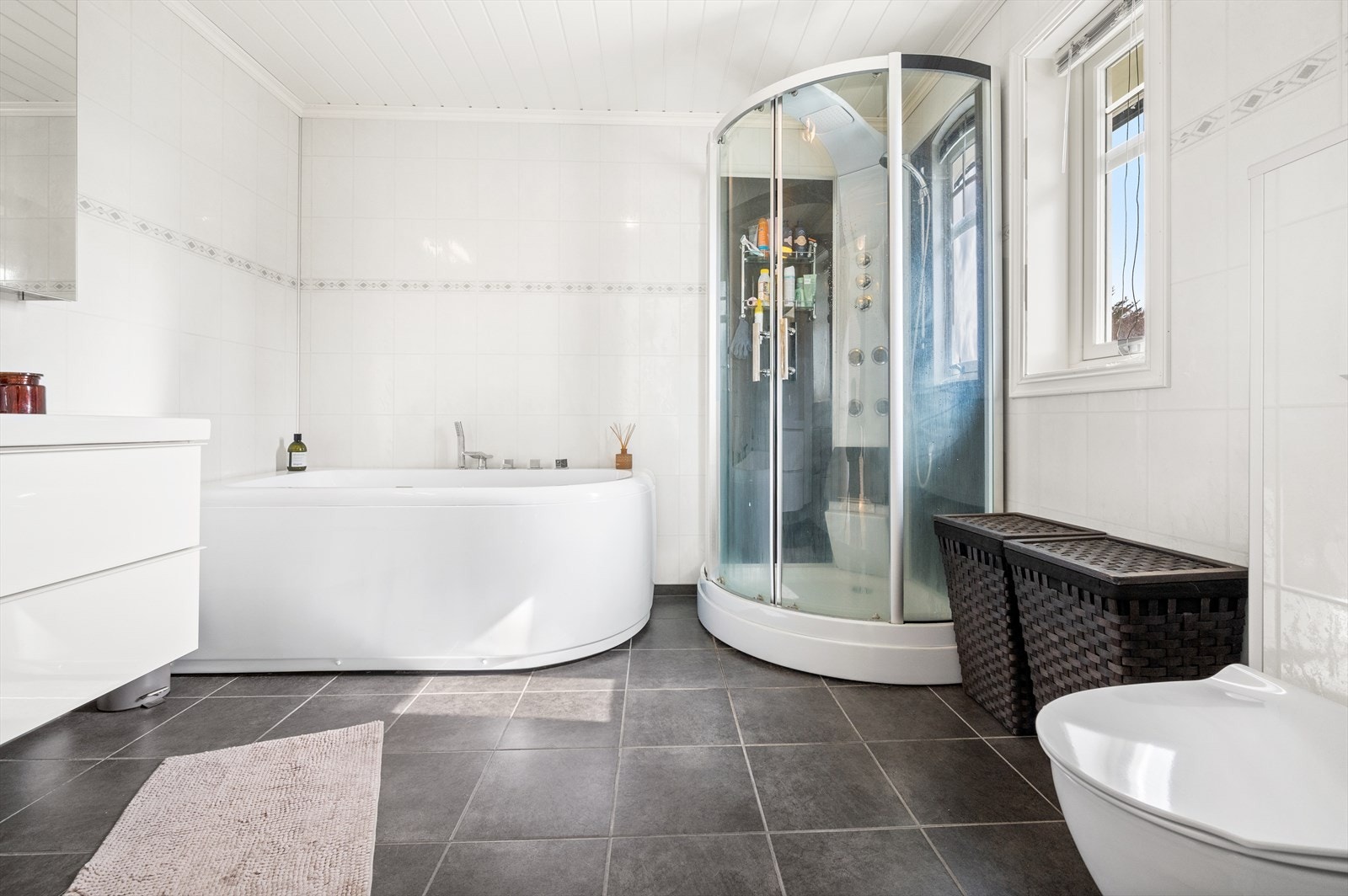 Flislagt gulv med varmekabel. Vegger kledd med baderomsplater. Dusjkabinett. Veggmontert toalett. Badekar Galleribilde