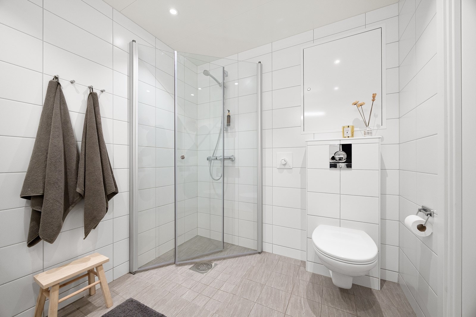 Lyst og moderne baderom med dusjhjørne, vegghengt toalett og stilrene overflater. Galleribilde