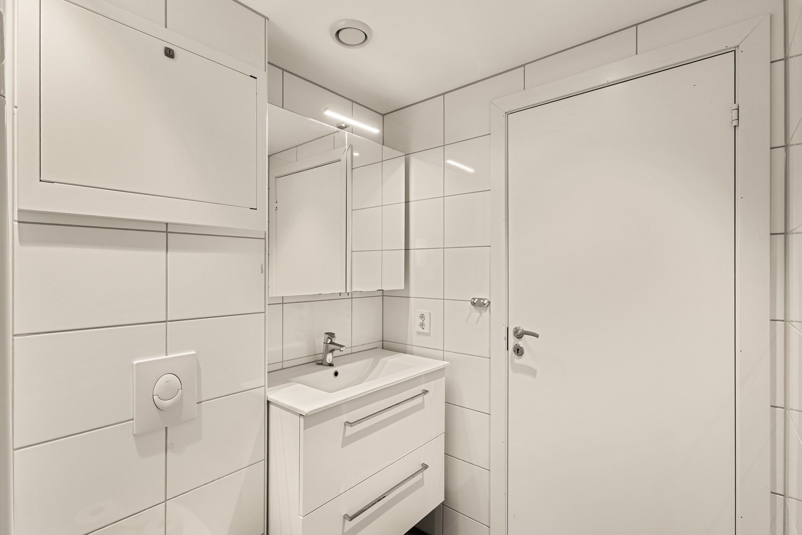 Badet er helfliset og inneholder servant, speilskap, vegghengt toalett, dusjhjørne og opplegg for vaskemaskin. Galleribilde