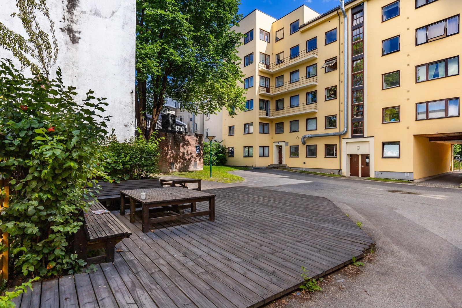 Fellesområde med trebenker og bord, omkranset av vegetasjon Galleribilde