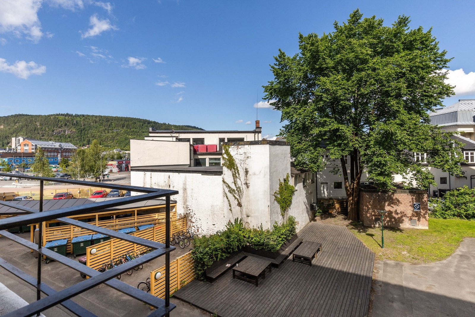 Utsikt over gårdsplass med sitteplasser, sykkelparkering og grøntområder. Galleribilde