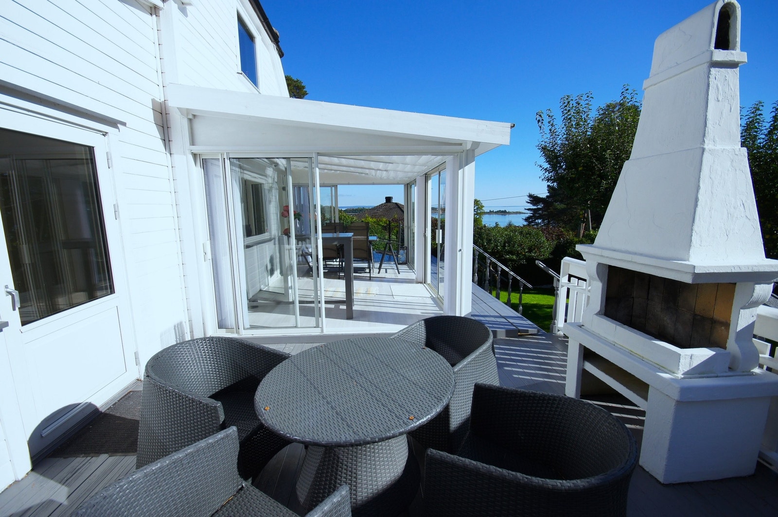 Vest terrassen med sittegruppe og ute peis og hagestua. Sjøutsikt. Galleribilde