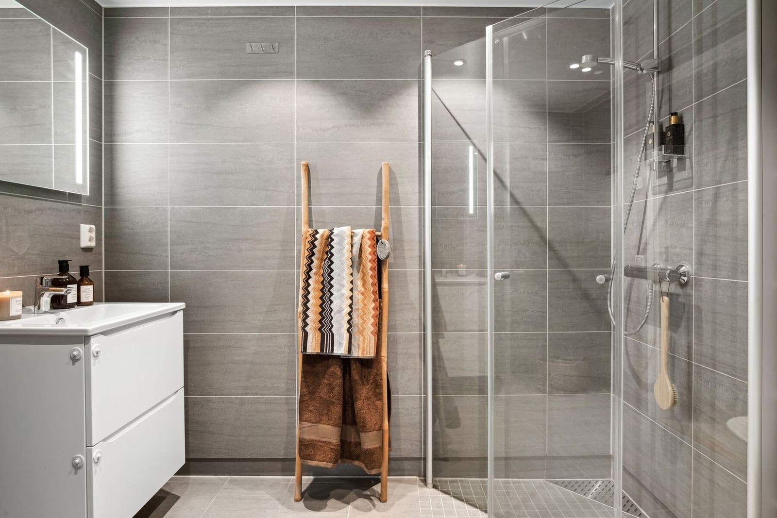 Moderne og stilrent baderom med elegante, grå fliser på vegger og gulv, som skaper en harmonisk og tidløs atmosfære. Galleribilde