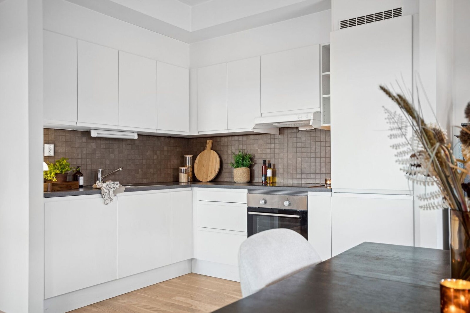 Kjøkkenet er innredet med hvite, rene fronter som står i flott kontrast til den mørke, sildemønstret flisen på veggen. Galleribilde