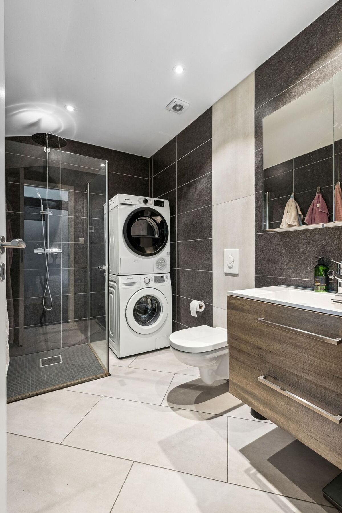 Lekkert baderom fra 2019 med innredning, servant, speil, veggmontert toalett, dusjhjørne og opplegg for vaskemaskin og tørketrommel. Galleribilde