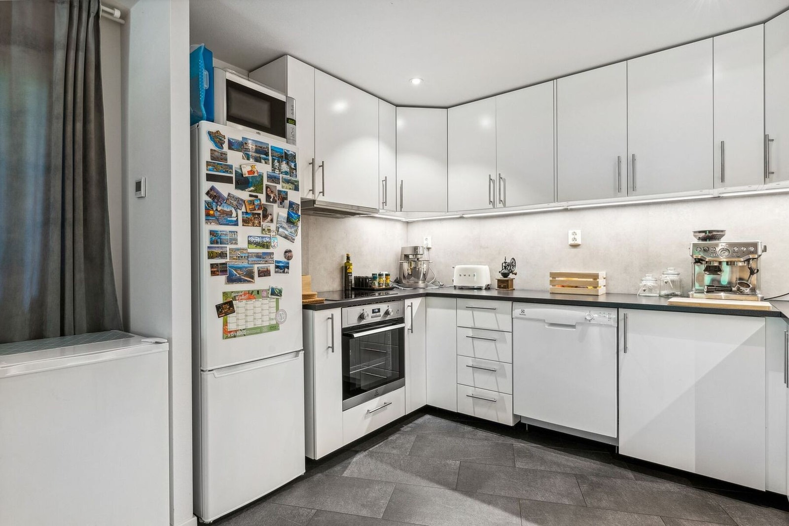 Lys kjøkkeninnredning med glatte fronter, benkeplater i laminat, oppvaskkum med ett-greps blandebatteri og ventilator over kokesonen. Galleribilde