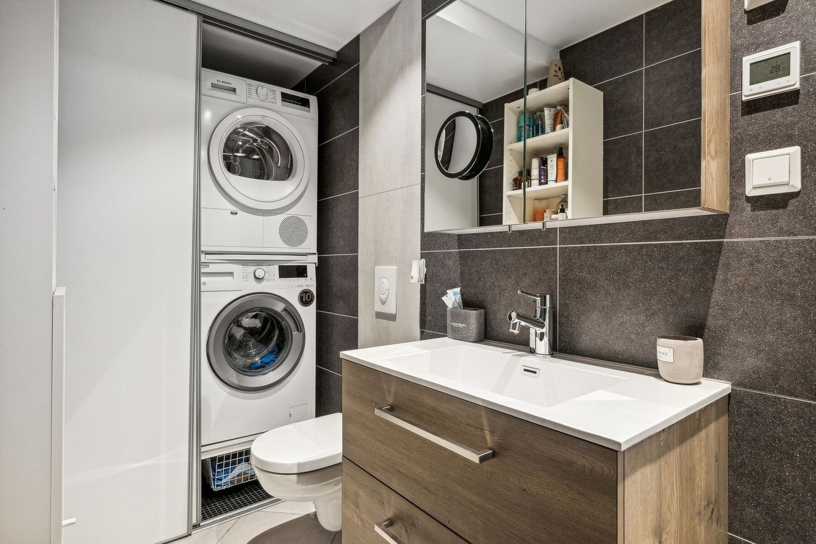 Pent baderom fra 2019 med innredning, speilskap, veggmontet toalett og opplegg for vaskemaskin og tørketrommel bak praktisk skyvevegg. Galleribilde