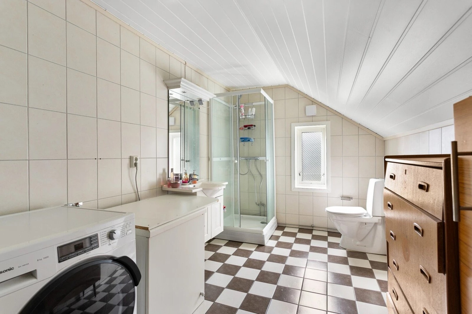 Bad med ukjent alder. Flislagt gulv og vegger. Vegghengt servantskap med heldekkende servant og ett-greps armatur. Speil over servant med overlys. Dusjkabinett med dusjarmatur. Gulvmontert toalett. Vaskemaskin. Galleribilde