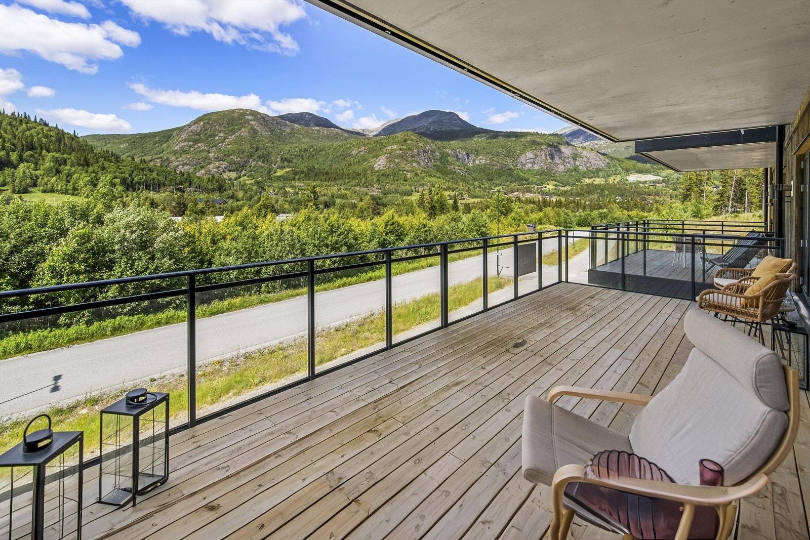 På gulvet er det lagt terrassebord som rammes inn av et luftig rekkverk av sort stål og glass. Balkongen i etasjen over danner et lunt og koselig overbygg som skjermer for sol og lett sommerregn. Galleribilde