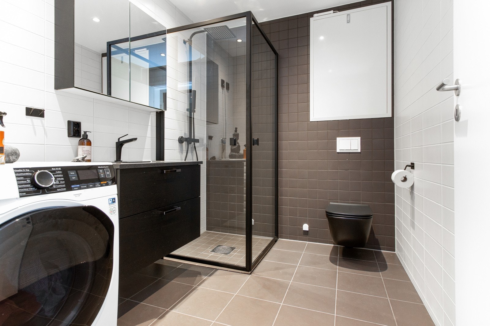 Dagene får en god start på et lekkert bad, der lysegrå gulvfliser kombineres med hvite og mørkegrå veggfliser i en annen størrelse. uj Galleribilde