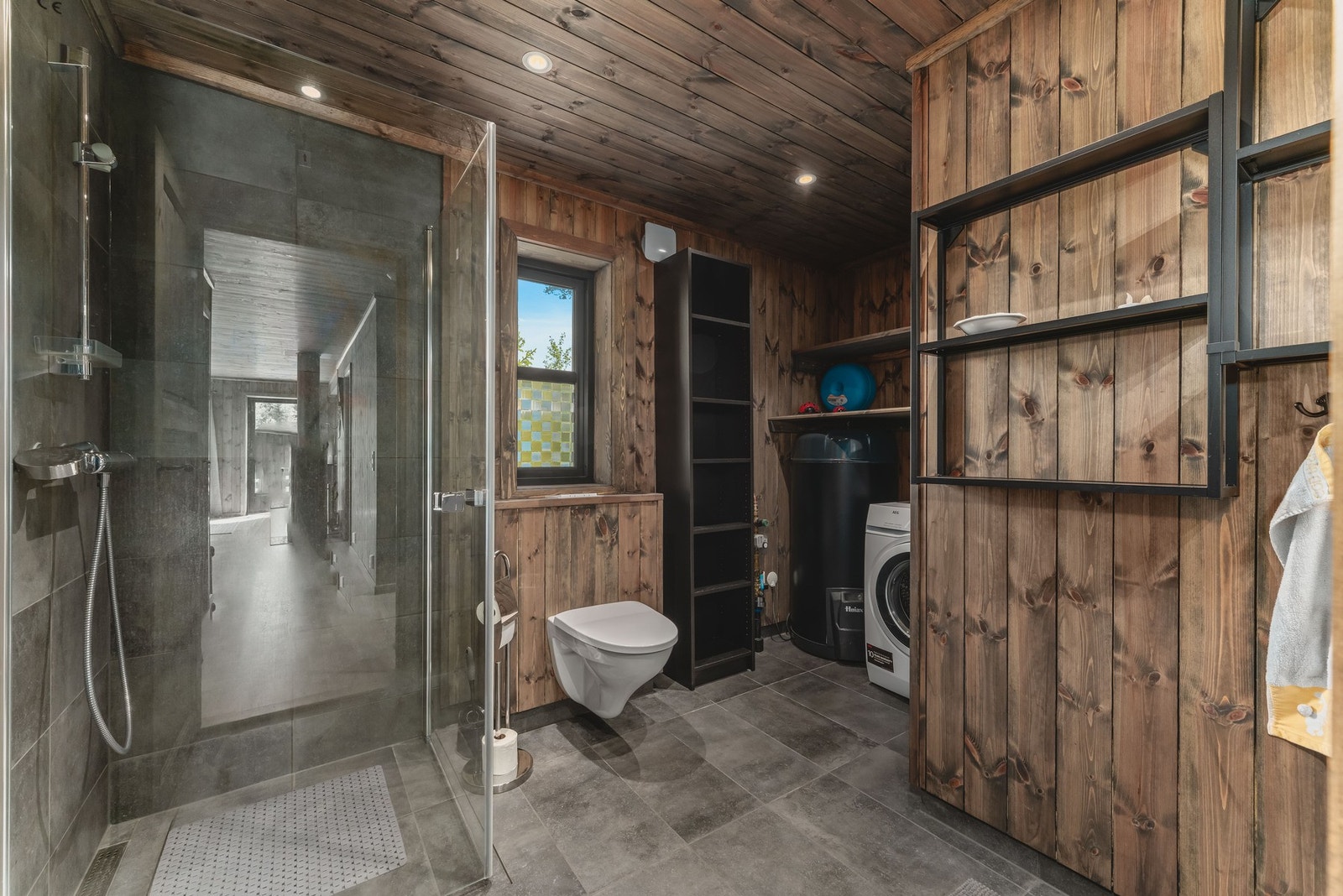 Badet er delikat og funksjonelt med fliser på gulvet, elektriske varmekabler og en kombinasjon av fliser og panel/tømmer på veggene. Galleribilde