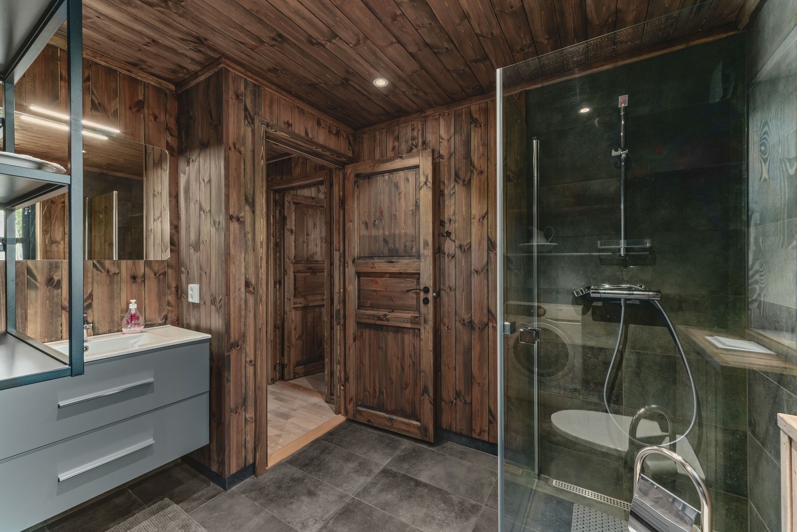 Her finner du dusjhjørne med dusjvegger, vegghengt toalett, servant med innredning og opplegg for vaskemaskin. Galleribilde