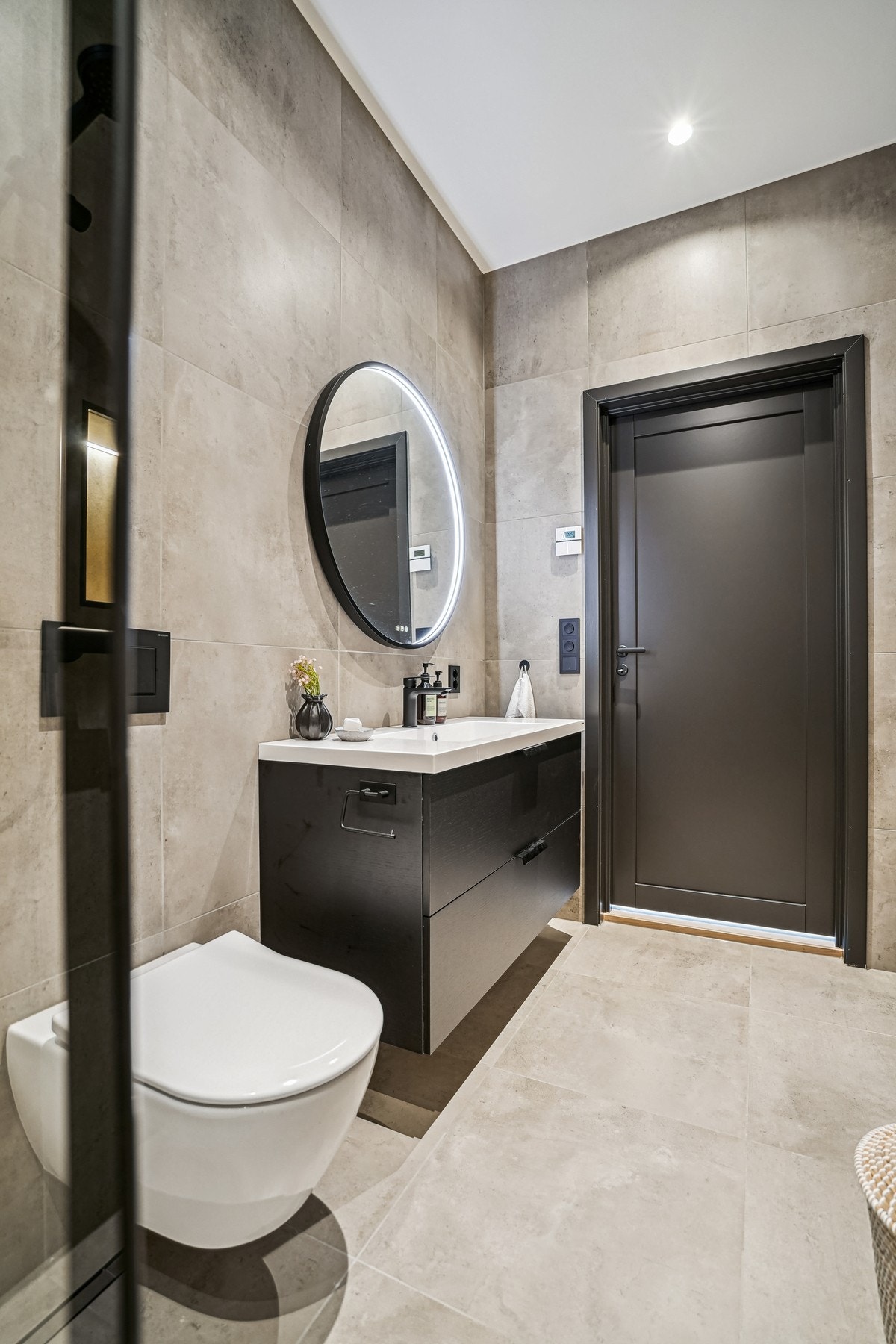 Innredet med dusjløsning, vegghengt toalett, moderne innredning og rundt speil med integrert belysning. Galleribilde