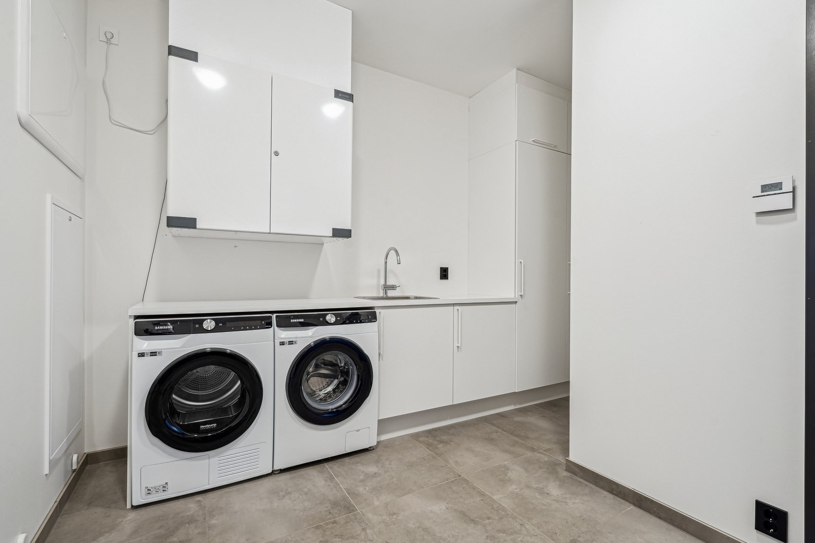 Romslig vaskerom med flislagt gulv med fjernvarme og malte flater på vegger. Innredet med opplegg for vaskemaskin, tørketrommel og innredning med skappplass. Galleribilde