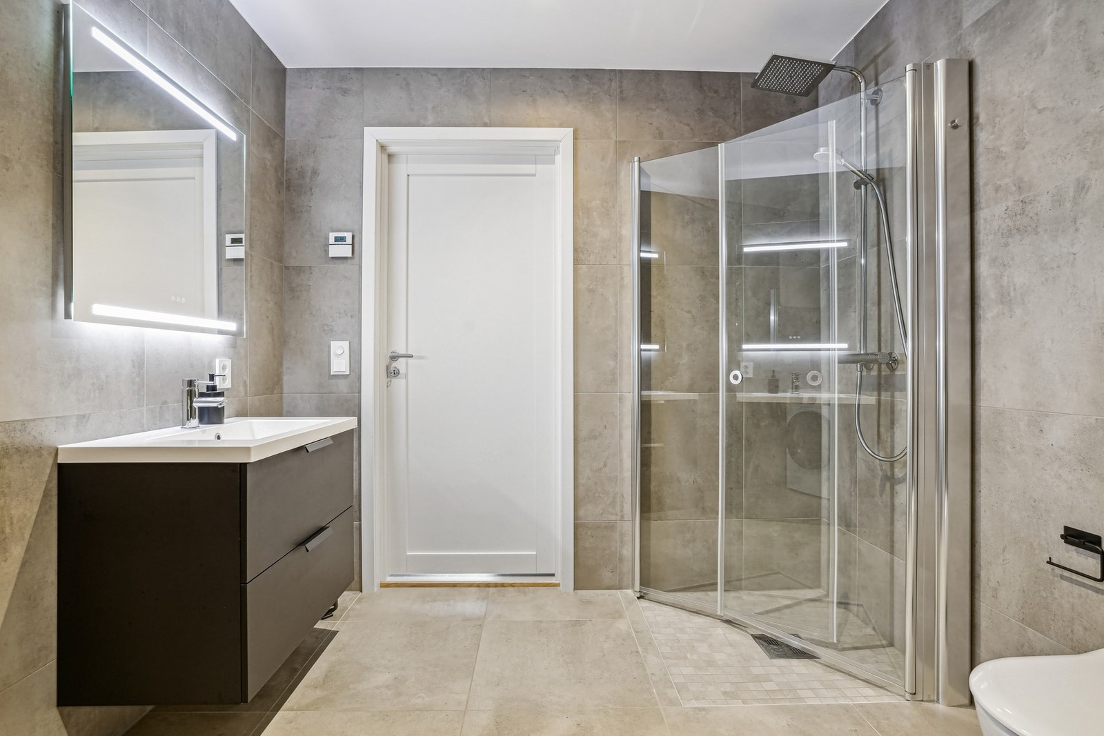 Innredet med vegghengt toalett, dusjhjørne, servantinnredning, speil med integrert belysning og opplegg for vaskemaskin. Galleribilde