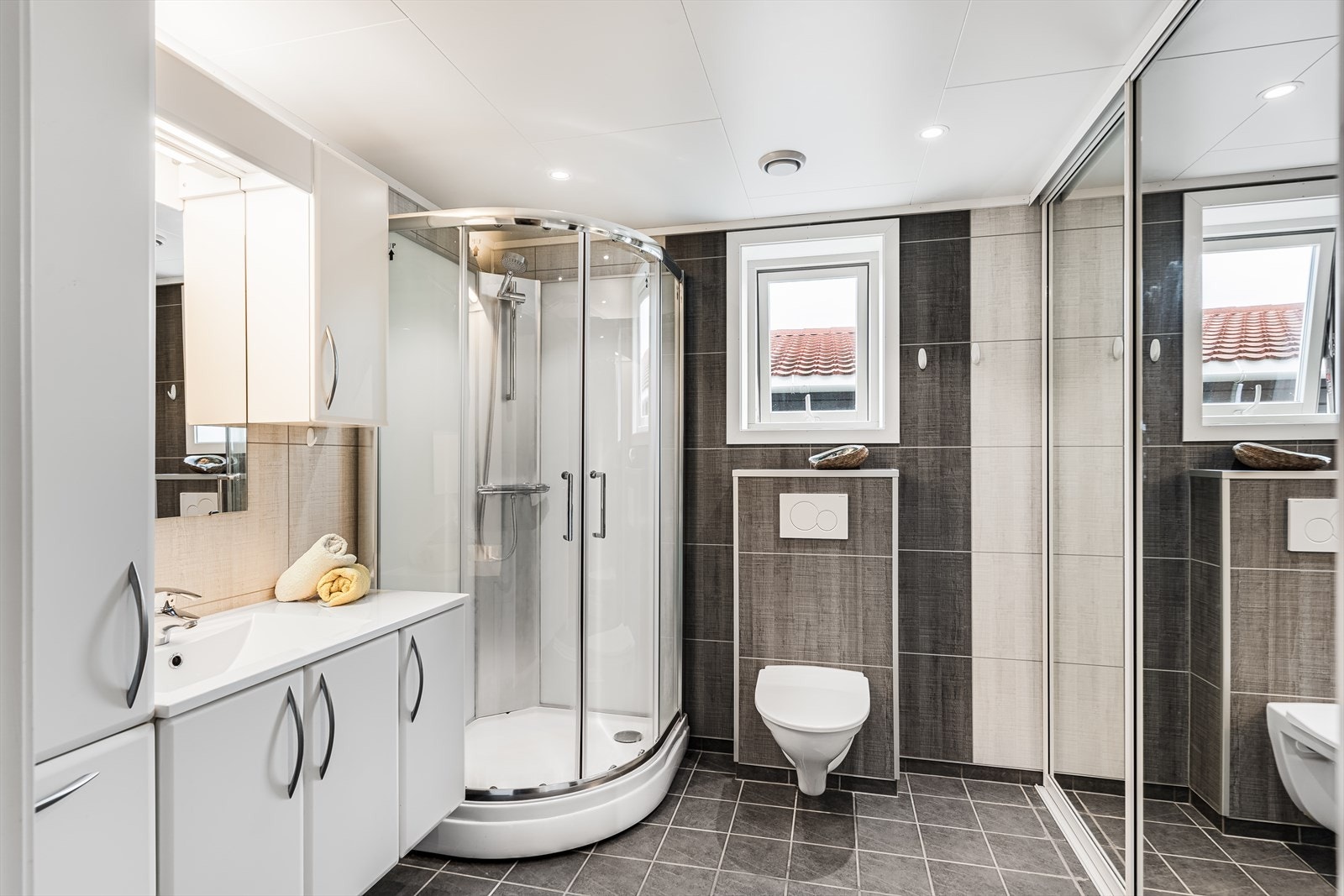 Baderom med flislagt gulv og varmekabler, våtromsplater på vegger og himlingsplater med downlights. Galleribilde