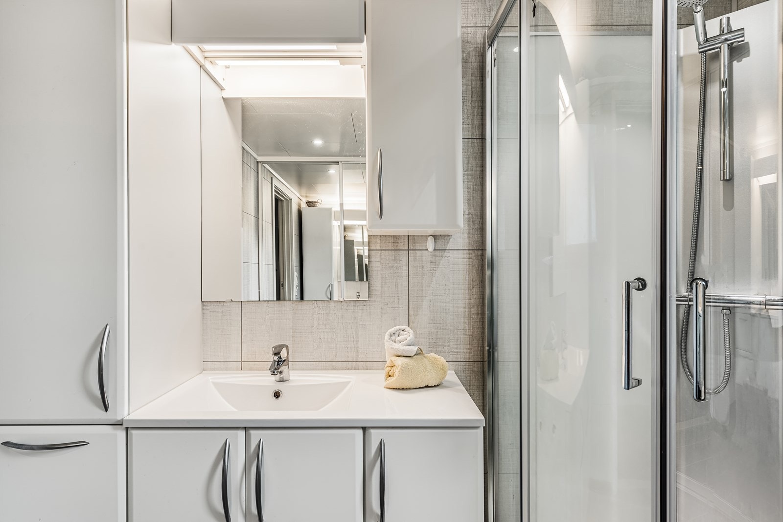 Hvit baderomsinnredning med heldekkende servant, over- og underskap, speil og belysning. Galleribilde