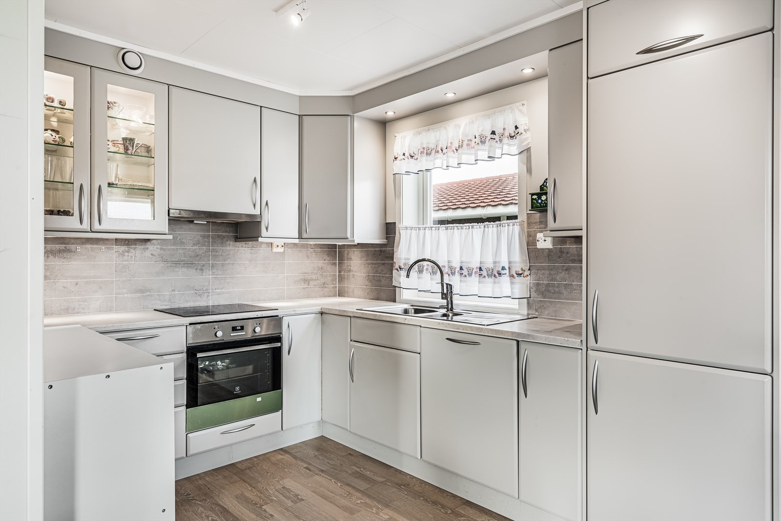 Lysegrå glatt kjøkkeninnredning i over- og underskap, samt laminert benkeplate med nedfelt oppvask kum i stål. Galleribilde