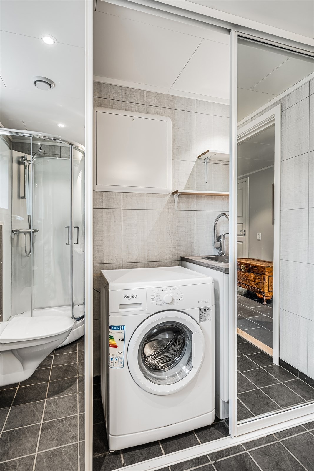 Varmtvannsbereder, opplegg for vaskemaskin og skyllekum nedfelt i skap bak skyvedør. Praktisk løsning med bad og vaskerom samlet. Galleribilde