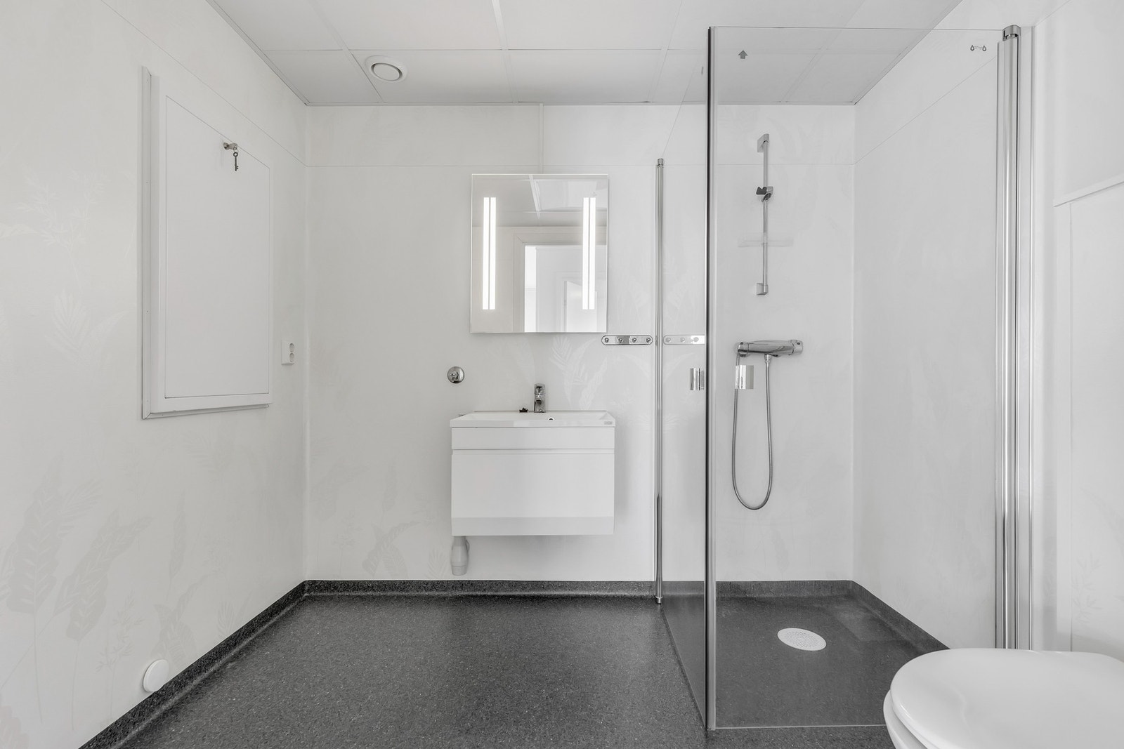 Dusjhjørne med dører av glass, vegghengt servantskap med overliggende servant, opplegg for vaskemaskin og tørketrommel på vegg. Galleribilde