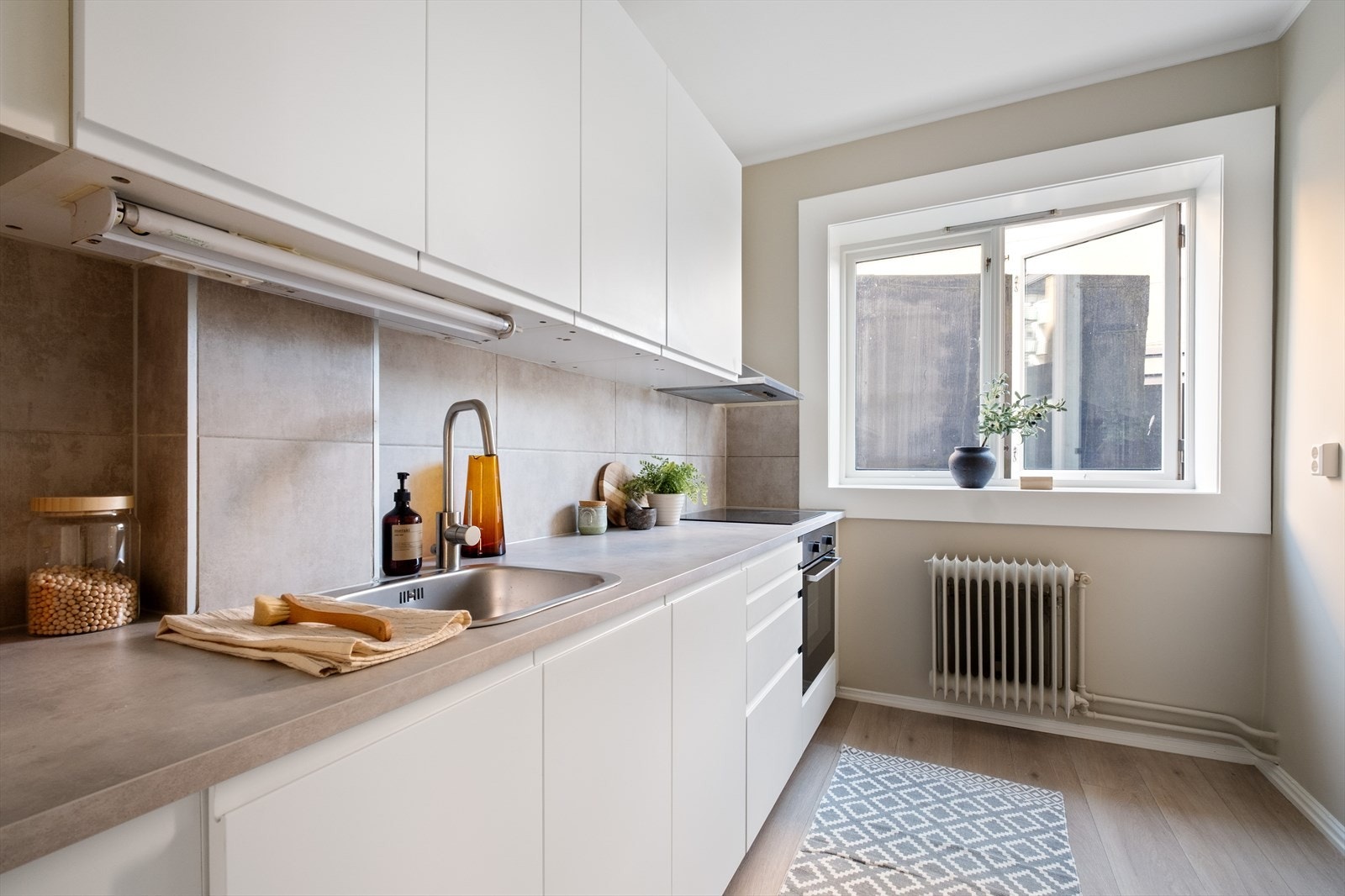 Pen kjøkkeninnredning fra IKEA med glatte fronter, soft close, laminat benkeplate med nedfelt kum, integrert oppvaskmaskin og komfyr. Kullfilter over koketopp. Galleribilde