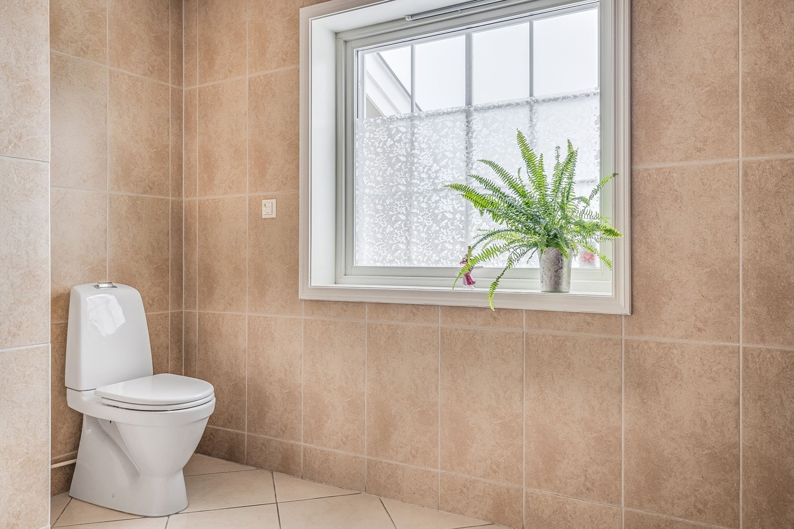 Baderommet har tidløse fliser på gulv og vegger, gulvvarme og et vindu som slipper inn dagslys. Galleribilde