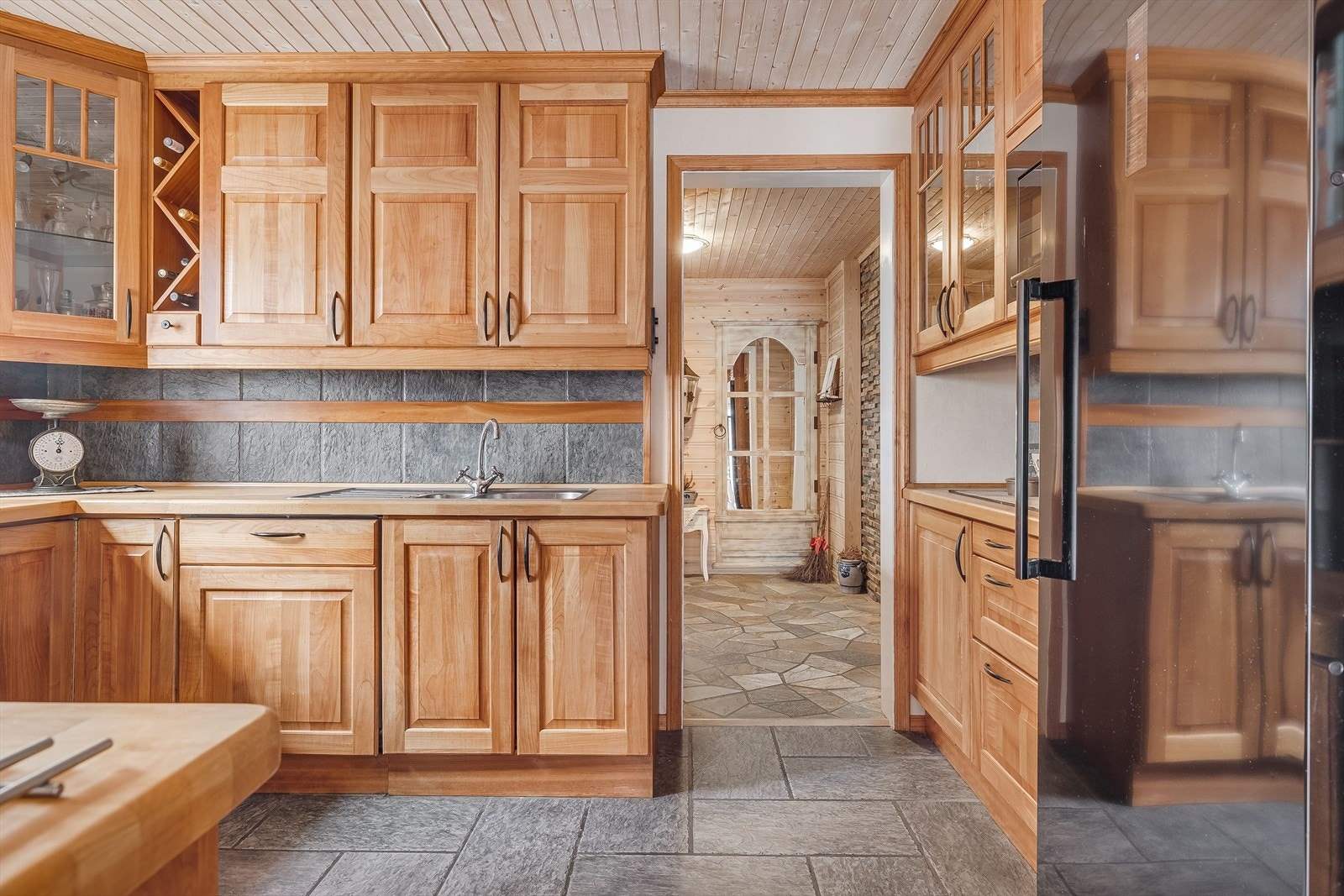 Pent kjøkken med takhøye overskap, fliser i benkeryggen og heltre benkeplate med nedfelt oppvaskkum. Galleribilde