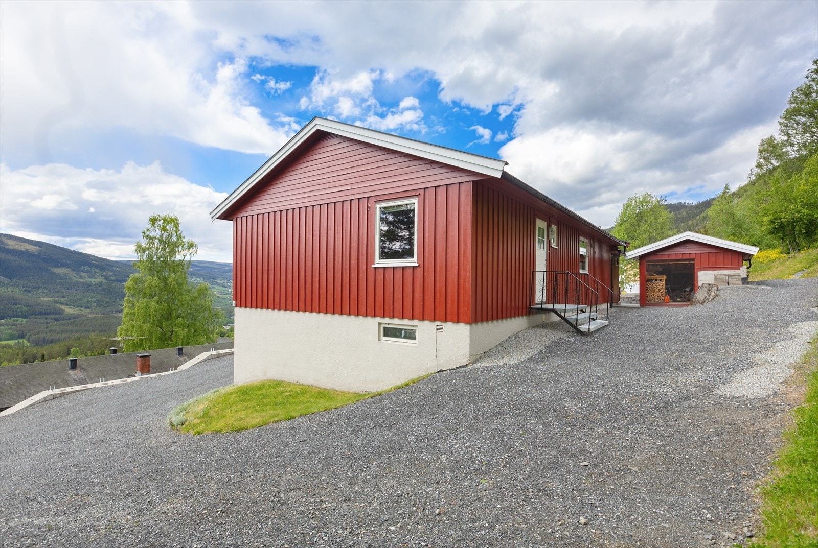 Tomt med opparbeidet hage med gressplen, ellers naturtomt i skårende/bratt terreng ved lauv/barskog. Galleribilde