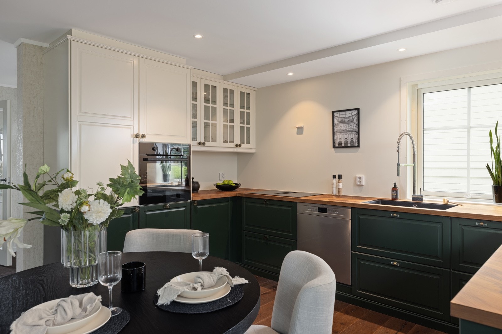 Innredningen er grønn med hvite overskap med profilerte fronter og en stilren laminat eik benkeplate med underlimt kum i svart. Galleribilde