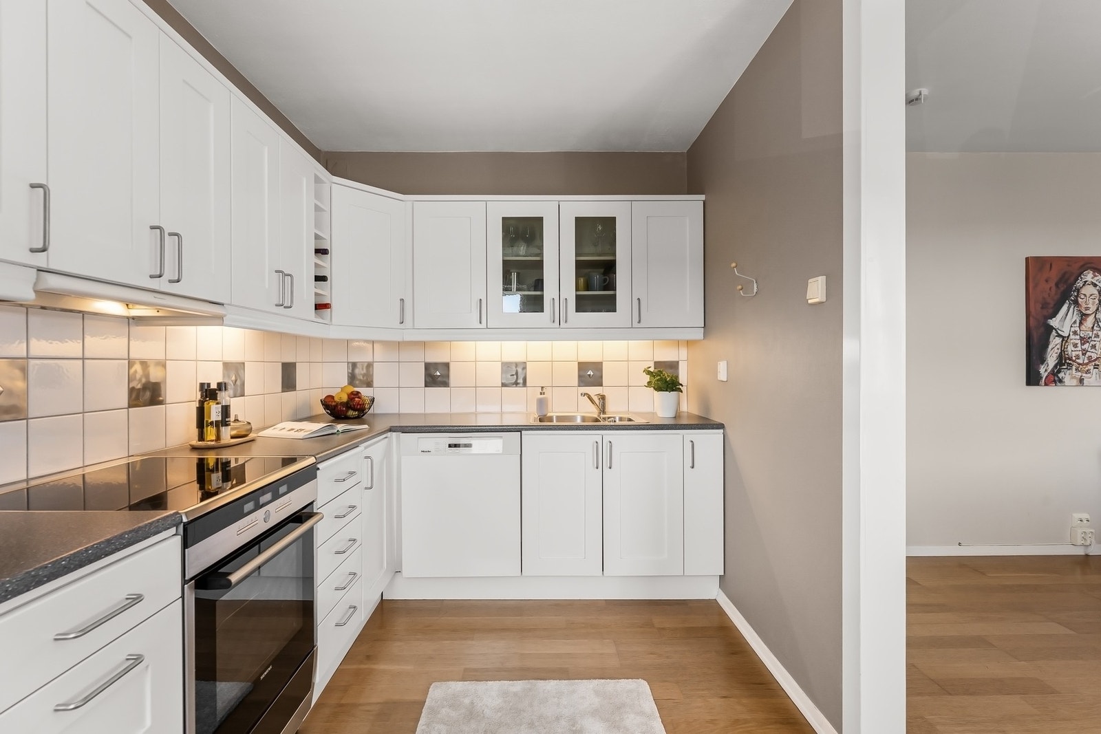 Kjøkkenet er innredet med hvite profilerte fronter, laminat benkeplate med nedfelt oppvaskkum, samt fliser på vegg over benk. Galleribilde