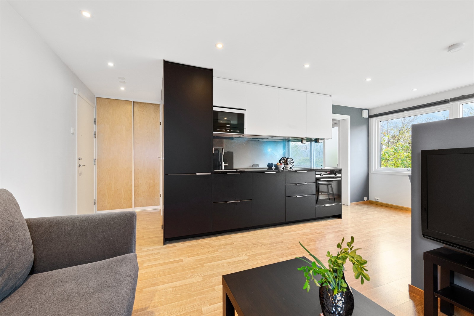 Kjøkkenet er plassert midt i leiligheten med mørke underskap og lyse overskap Galleribilde