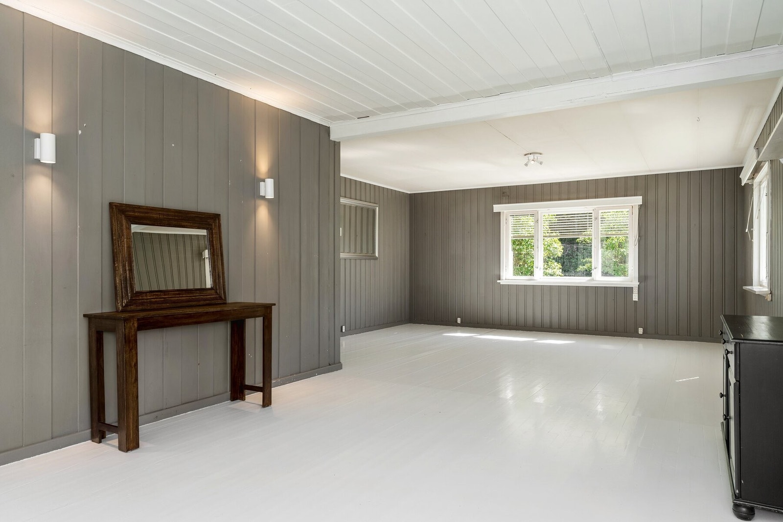 Gulvbord av tre er malt i en lys gråtone, i kombinasjon med panelvegger holdt i en mørkere gråfarge. Galleribilde