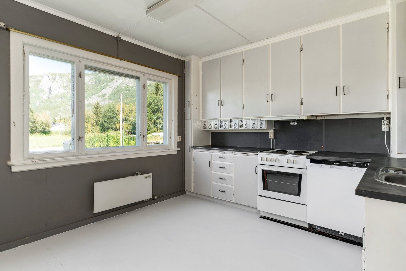 Et eldre kjøkken har malte gulvbord i tre, og maten lages med naturen som vakkert bakteppe. Galleribilde