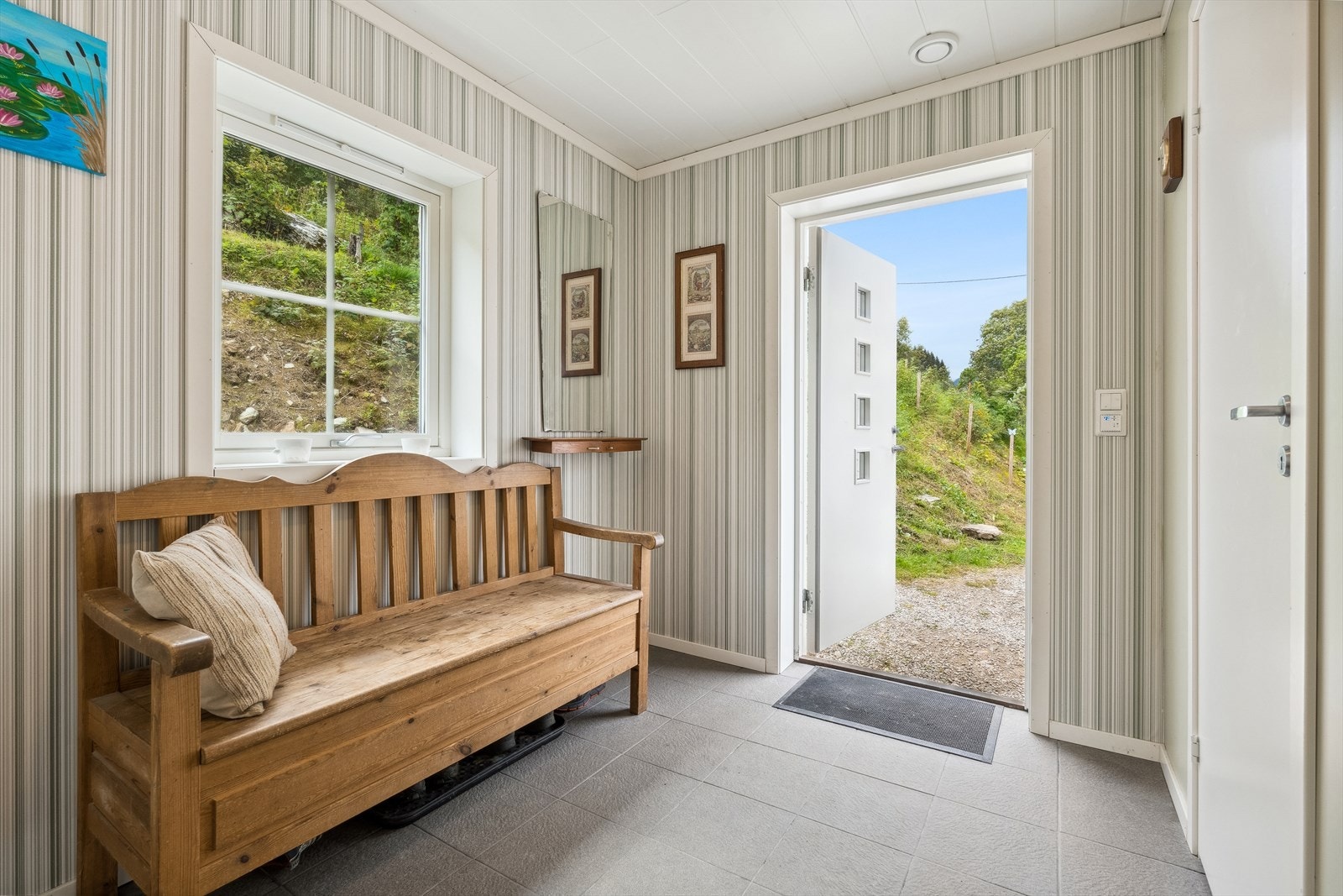 Velkommen inn i en romslig gang med flislagte gulv, Det er varmekabler i gulvet. Her er det god plass til å etablere ulike garderobeløsninger etter eget behov. Fra gangen har man også direkte adgang til bod. Galleribilde