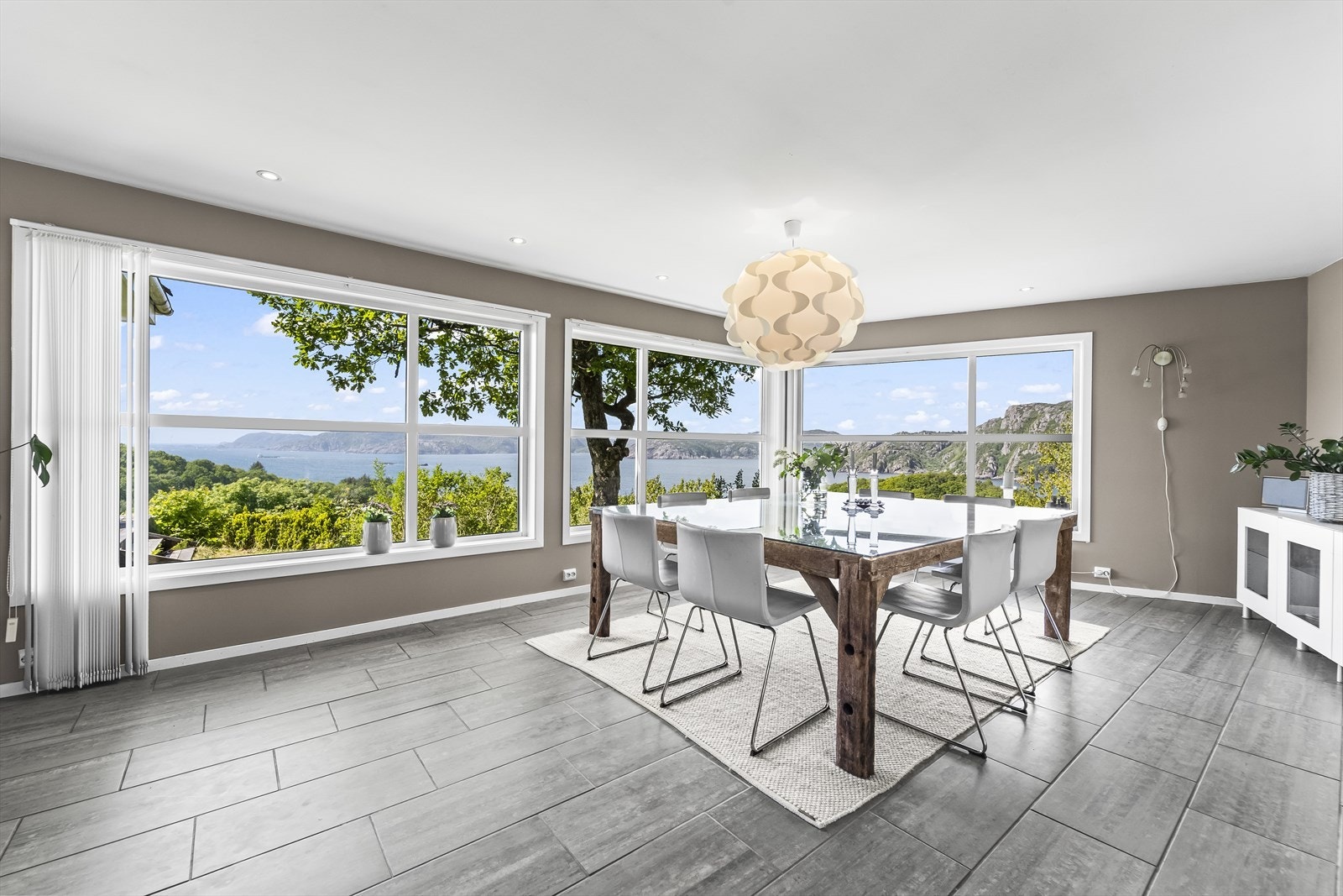 Lys og moderne spisestue med store vindusflater som rammer inn den vakre utsikten mot fjell og grønt landskap. Her kombineres stilrent interiør med naturens egen dekor. Galleribilde