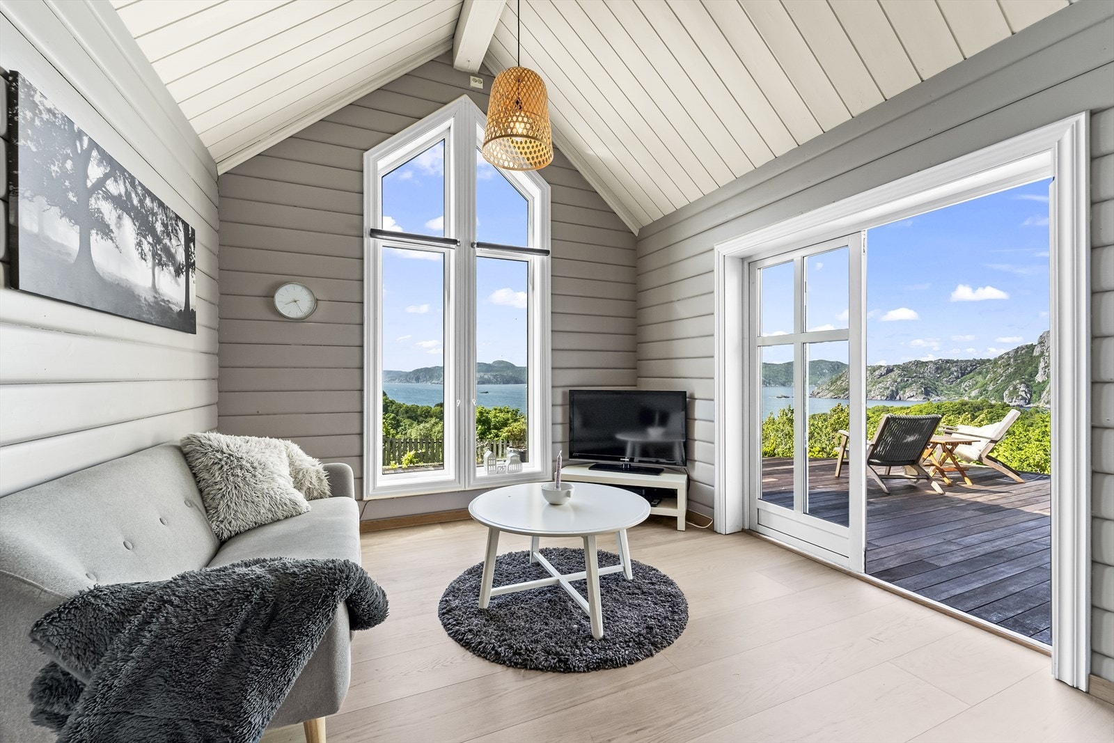 Spektakulær utsikt over sjø og fjell fra tv-stue med store vinduer og direkte utgang til en solrik terrasse. Galleribilde