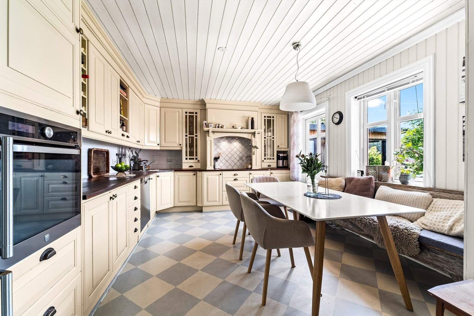 Dette romslige kjøkkenet kombinerer klassisk stil med moderne komfort. De kremfargede skapene og det mørke treverket på benkeplatene skaper en varm og tidløs atmosfære, mens det rutete gulvet gir rommet karakter. Galleribilde