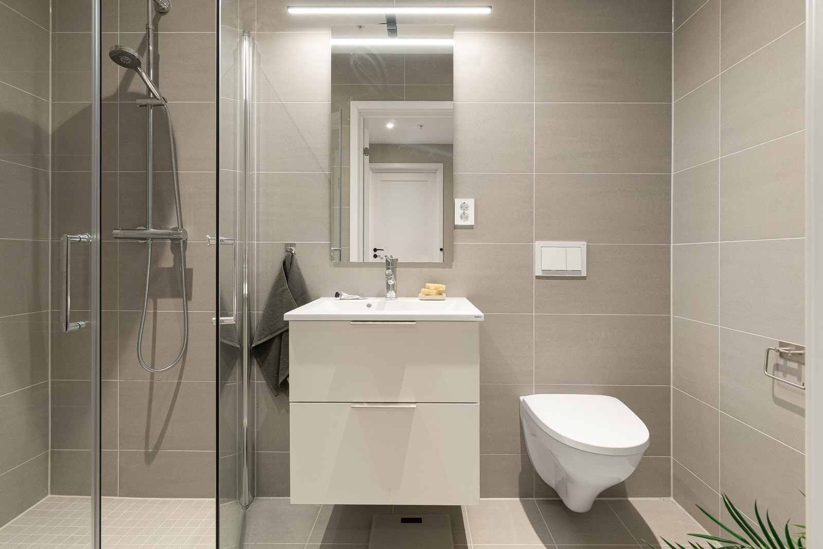 Leilighetens første bad er stilrent og moderne med flislagt gulv og elektrisk gulvvarme. Downlights i himlingen gir et godt og behagelig lys. Galleribilde