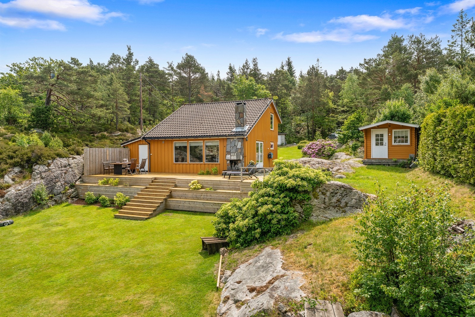 Tomten er meget pent opparbeidet på begge sider av hytten med fine plener og flott beplantning Galleribilde