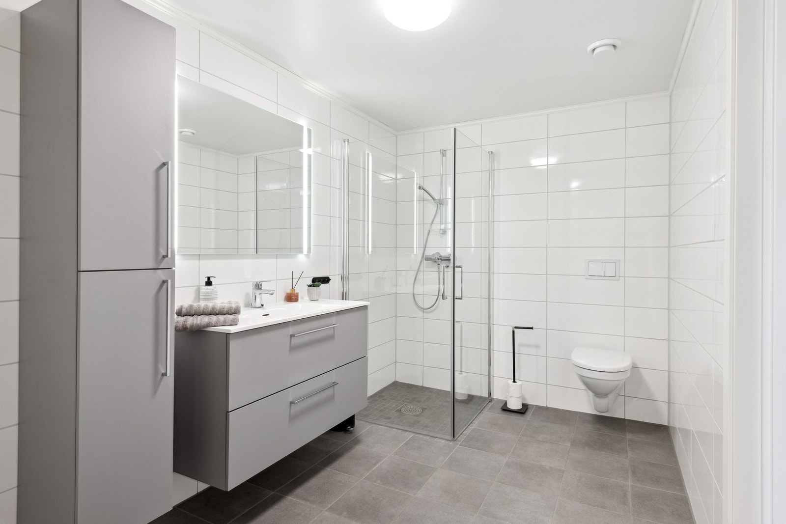 Flislagt bad med vannbåren gulvvarme, dusjhjørne og godt med oppbevaringsplass i skuffer og skap Galleribilde