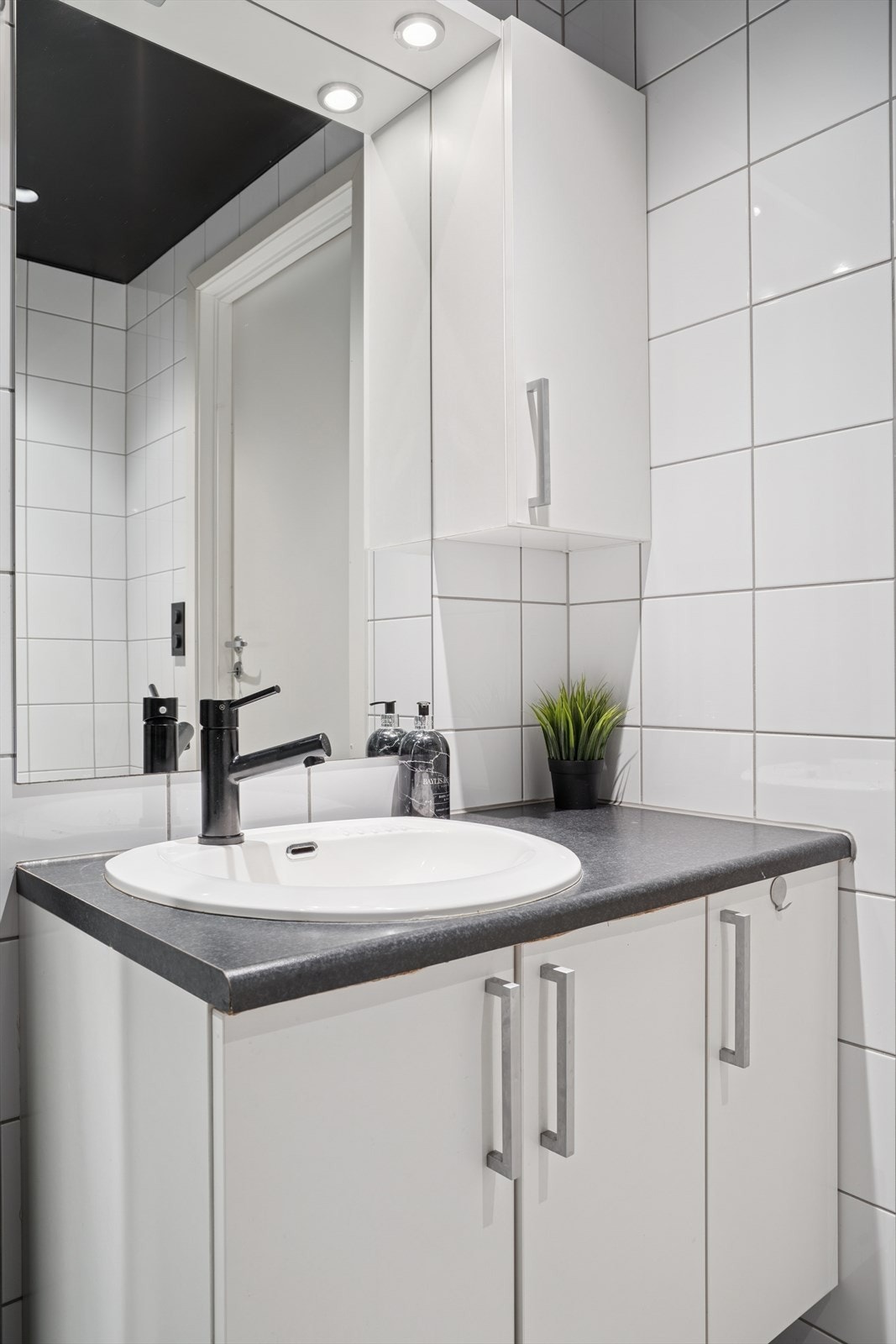 Leilighetens bad har en tidløs utførelse med hvite fliser på veggene og mørke fliser på gulvet. Galleribilde