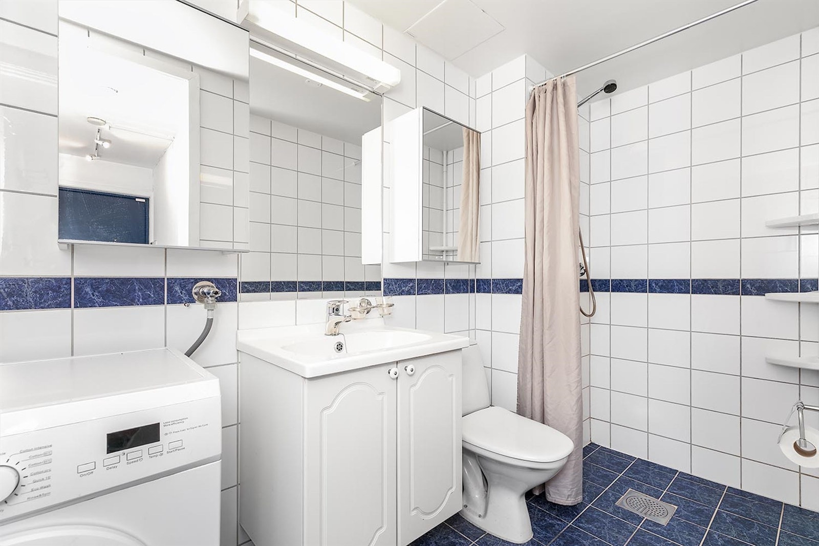 Lyst flislagt bad med lys innredning, opplegg for vaskemaskin og gulvvarme Galleribilde