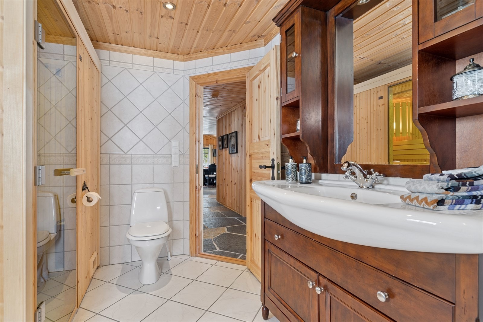 Baderomsinnredningen i eik består av en heldekkende servant med både skuffer og skap for god oppbevaring. Dusjsonen er utstyrt med glassdører og toalett. Galleribilde