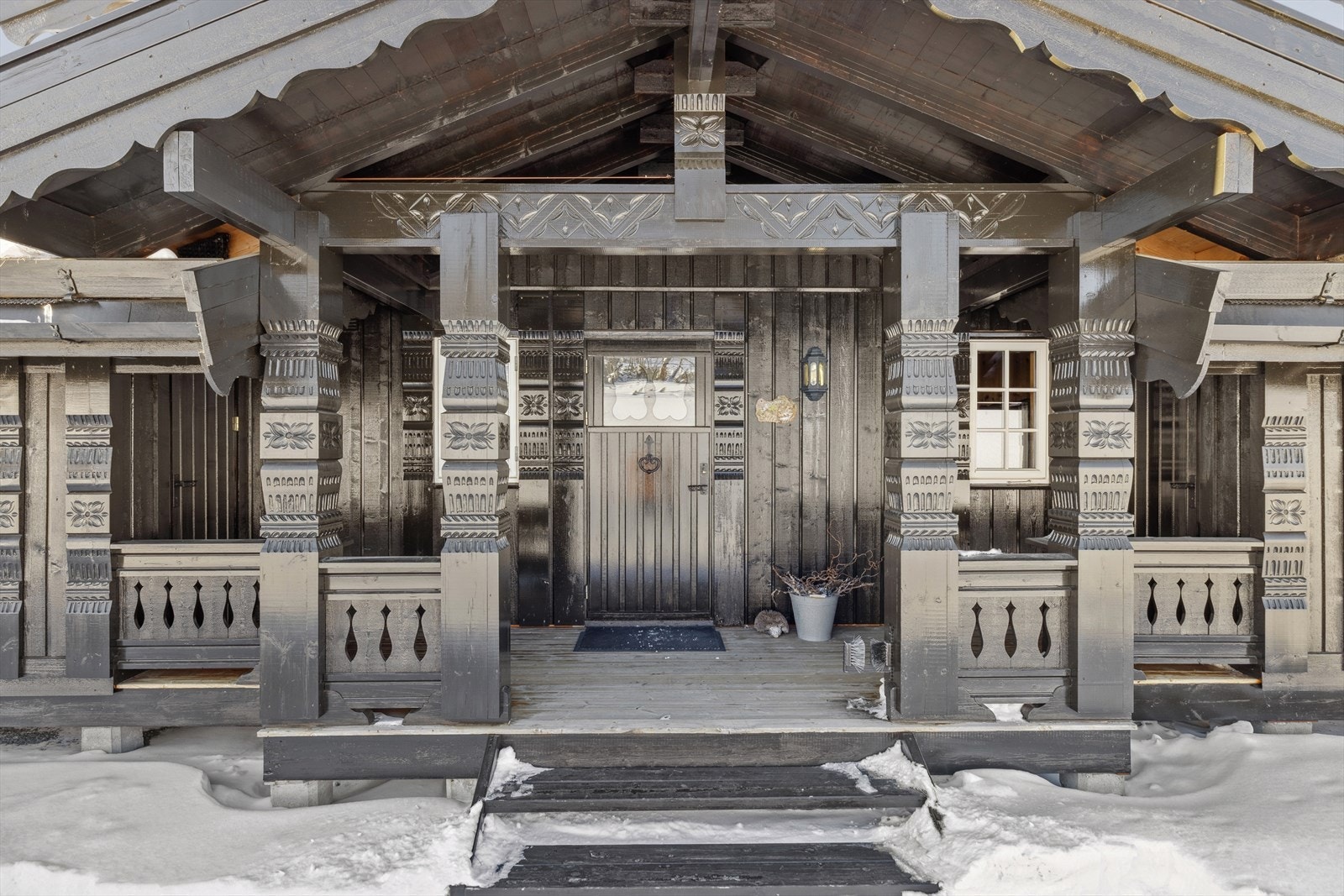 Hytta har et overbygget inngangsparti med platting. Det er bod på hver side av inngang. Galleribilde