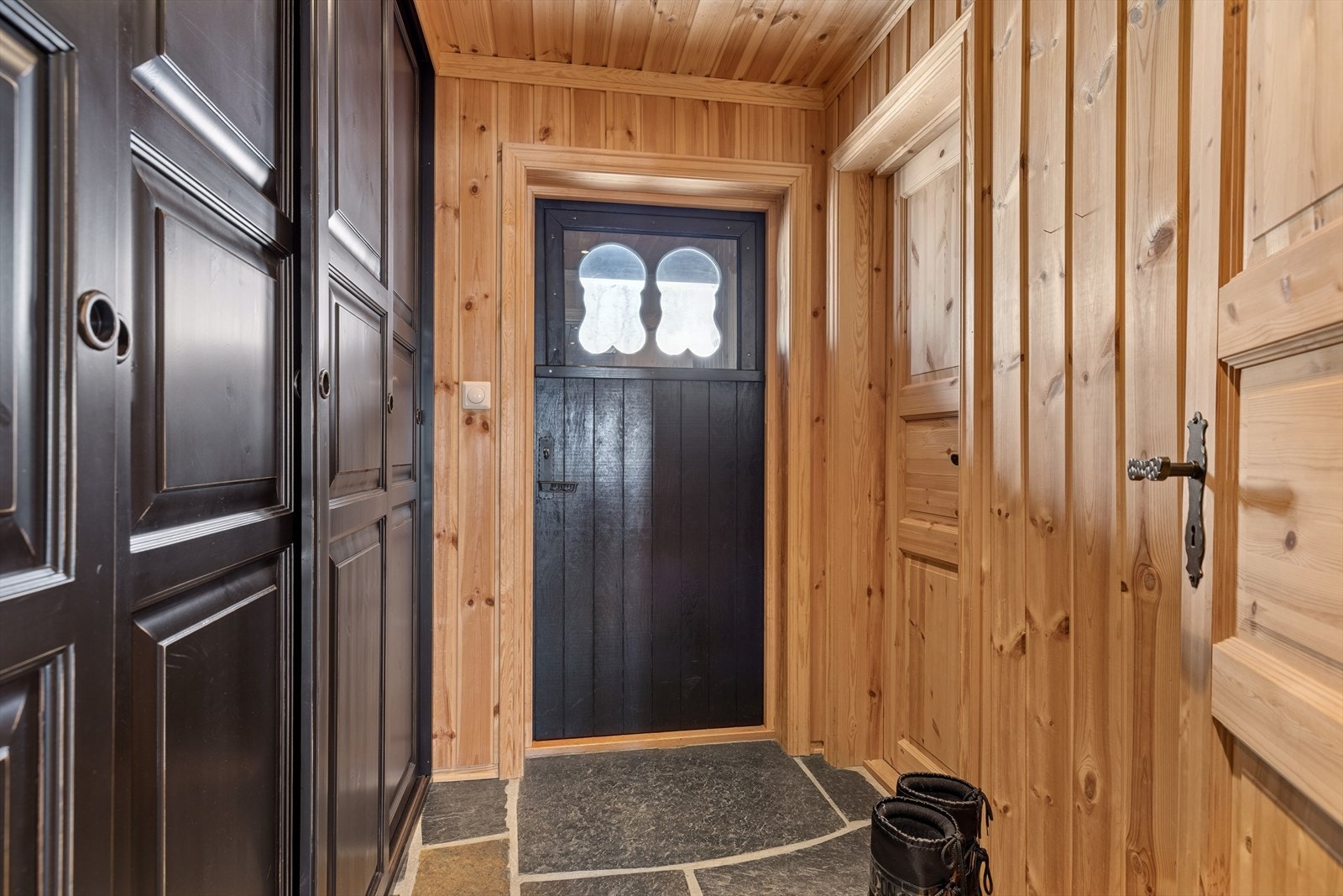 Gangen er innbydende, og står i stil til de øvrige rommene i hytta. På gulvet er det skiferfliser med vannbårenvarme i gulv. Veggene er kledd med panel. Det er montert downlights i himling. Det er stort garderobeskap med skyvedører i entre. Galleribilde